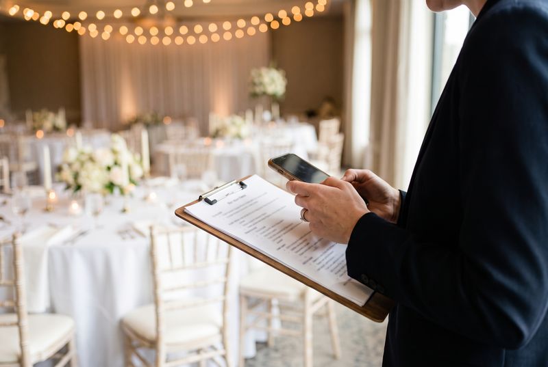 A coordinator with a run-sheet and phone as a wedding reception is set up