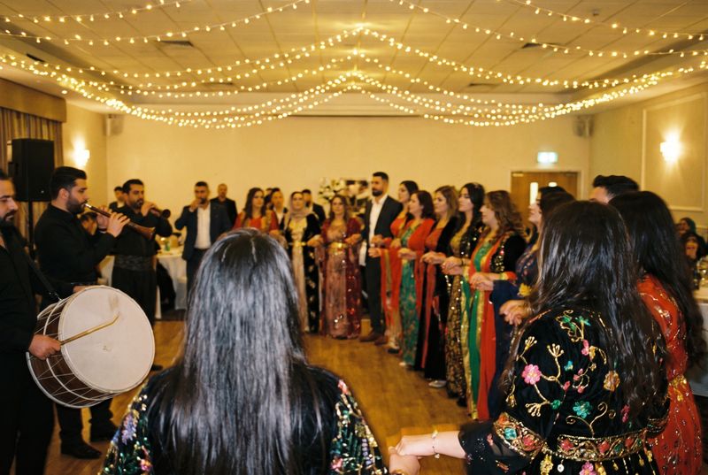Guests in colourful traditional dress dancing the halay beside a davul drummer