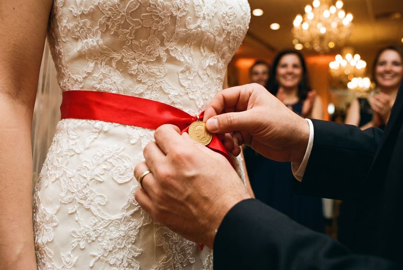 A guest pinning a gold coin onto the bride's red sash during the takı